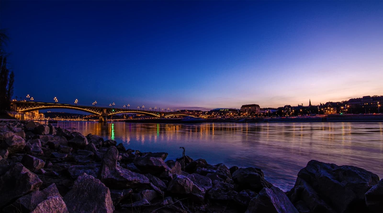 A Margit híd és Budapest kivilágított látképe kék órában, a Dunán tükröződve